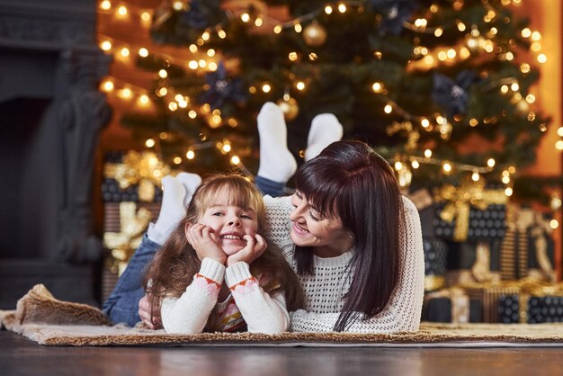 Kleines Mädchen und ihre Mutter liegen zusammen im weihnachtlich dekorierten Raum auf dem Boden.