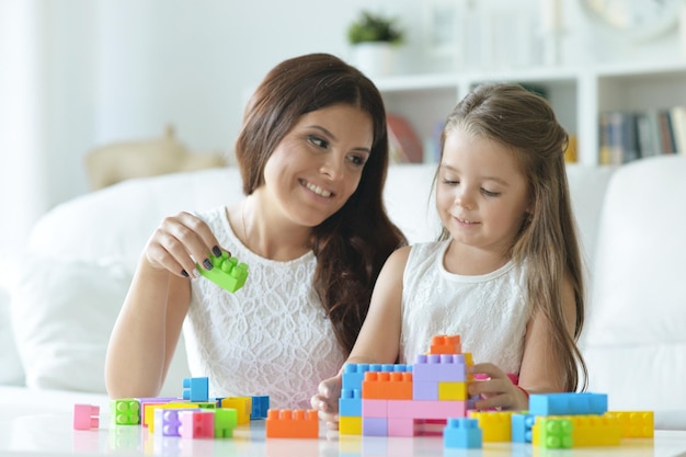 Kleines Mädchen und ihre Mutter spielen zu Hause mit bunten Plastikblöcken