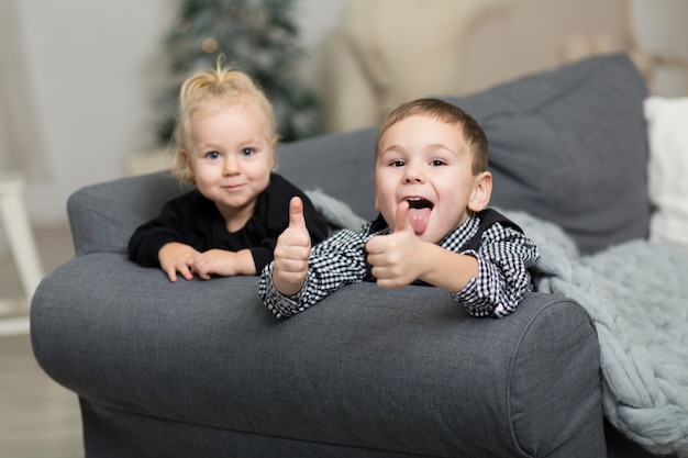 Kleines Mädchen und Junge, die t auf der Couch bedeckt mit einer grauen gestrickten Decke und einem Lächeln liegt.