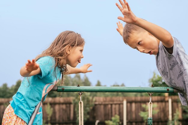 Kleines Mädchen und Junge täuschen und machen Grimassen gegenüber Freunde haben Spaß auf dem Spielplatz Lustige Gesichtsausdrücke