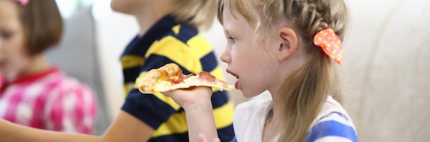 Kleines Mädchen und Kinder halten ein Stück Pizza in ihren Händen.