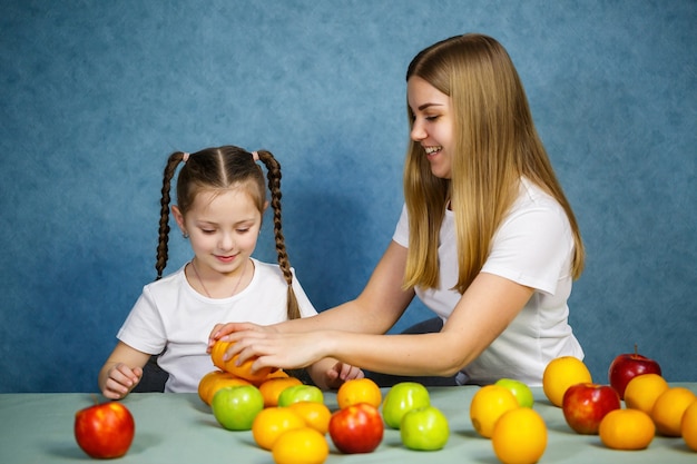 Kleines Mädchen und Mama spielen mit Früchten und albern herum. Sie tragen T-Shirts