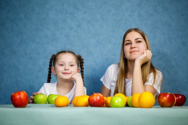 Kleines Mädchen und Mama spielen mit Früchten und albern herum. Sie tragen T-Shirts