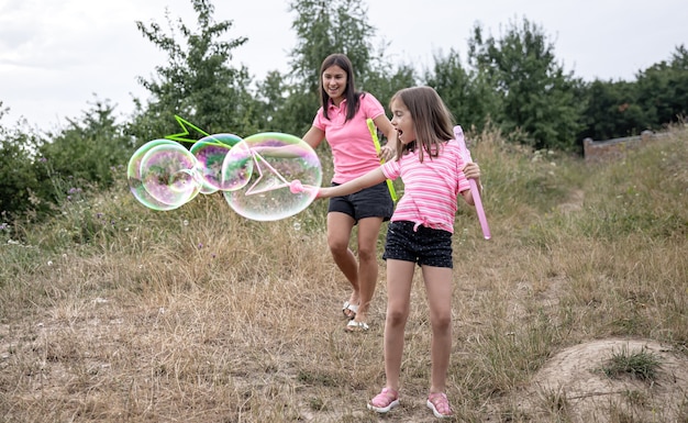 Kleines Mädchen und Mama spielen mit großen Seifenblasen in der Natur.