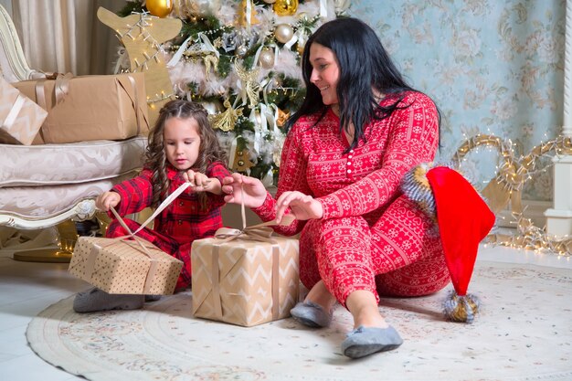 Kleines Mädchen und Mutter, die Geschenke nahe Weihnachtsbaum öffnen.