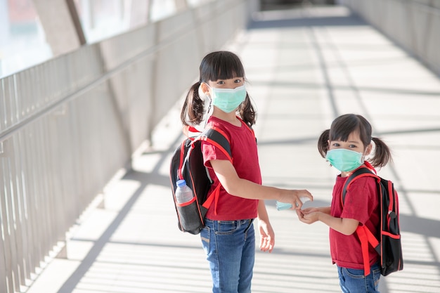 Kleines Mädchen und Schwester mit Gesichtsmaske, die während des Ausbruchs des Coronavirus zur Schule gehen. Sicherheitsmaske zur Krankheitsprävention. Mutter und Kind in der Schule während der Covid-19-Pandemien.