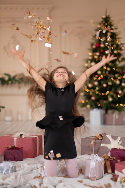 Kleines Mädchen wirft Konfetti. Weihnachtszauber. Freudige Momente einer glücklichen Kindheit.