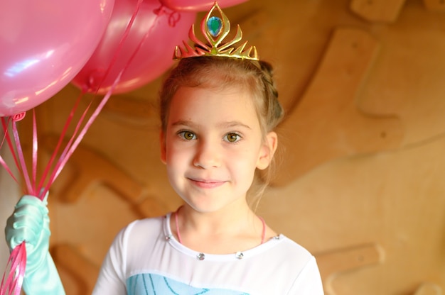 kleines Mädchen zu Hause in einem Eisprinzessinkostüm mit Krone und Luftballons feiert ihren Geburtstag
