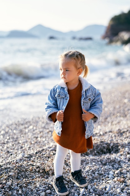 Kleines nachdenkliches Mädchen steht auf einem Kieselstrand