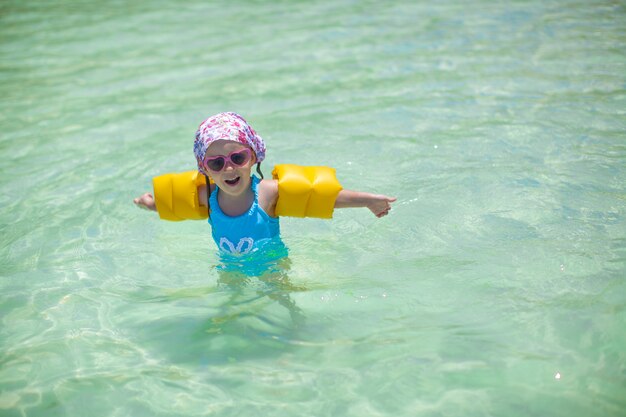 Kleines nettes glückliches Mädchen am Badeanzug hat Spaß im Meer