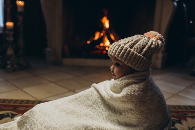 Foto kleines nettes mädchen, das nahe kamin sitzt, spaß in der winterzeit lächelt und hat. weihnachten, neues jahr, winterkonzept