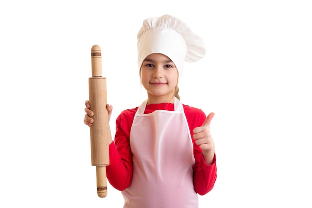 Kleines nettes Mädchen im Hemd mit weißer Schürze und Kochmütze auf weißem Hintergrund im Studio