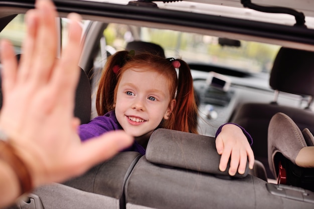 Kleines nettes Mädchen mit dem roten Haar lächelnd am Autoinnenraum