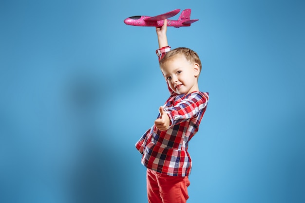 Kleines nettes Mädchen mit einem Spielzeugflugzeug, das sich ihren Daumen zeigt.