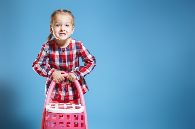 Kleines nettes Mädchen mit Spielzeugkoffer auf blauem Hintergrund.