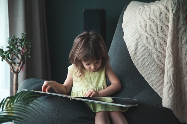 Kleines niedliches Baby, das ein Buch zu Hause liest, das auf einem Sitzsack sitzt