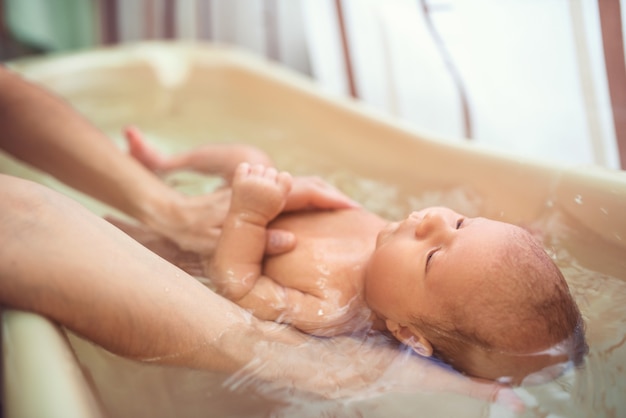 Kleines niedliches Baby mit großen Augen badet in warmem Wasser in den Händen einer fürsorglichen Mutter