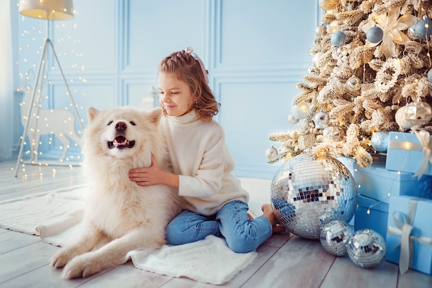 Kleines niedliches Mädchen mit einem weißen Malamute-Hund nahe Weihnachtsbaum.