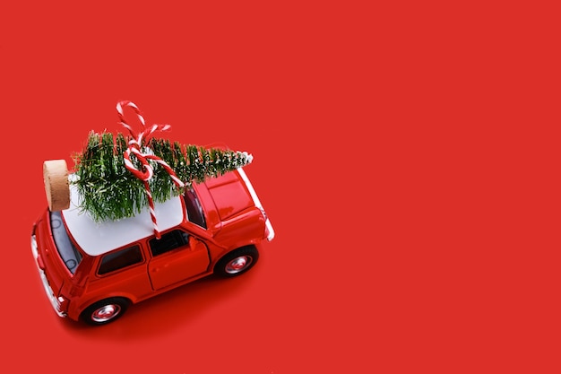 Kleines rotes Spielzeugauto und Weihnachtsbaum auf Rot. Draufsicht