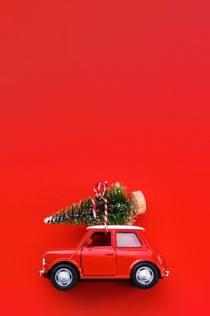 Kleines rotes Spielzeugauto und Weihnachtsbaum auf Rot.