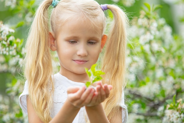 Kleines schönes Kindermädchenporträt mit einem jungen grünen Sprössling in ihren Händen