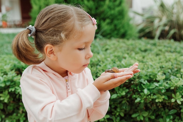 Kleines schönes Mädchen, das eine große Schnecke auf ihrer Hand hältKinder und Tiere lieben die Haustierpflege