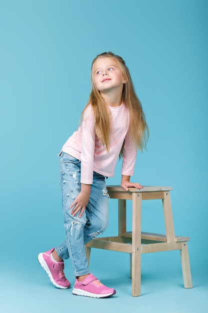 Kleines schönes Mädchen in rosa Pullover und Jeans posiert im Studio