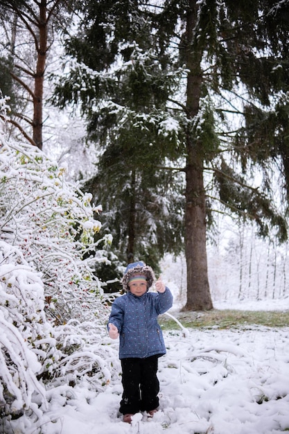 Kleines schönes Mädchen in Winterkleidung, das allein mitten in einem verschneiten Wald steht