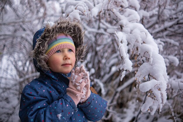 Kleines schönes Mädchen in Winterkleidung, das allein mitten in einem verschneiten Wald steht