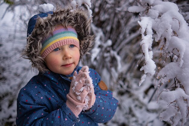 Kleines schönes Mädchen in Winterkleidung, das allein mitten in einem verschneiten Wald steht