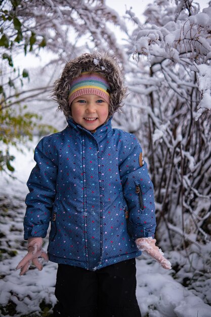 Kleines schönes Mädchen in Winterkleidung, das allein mitten in einem verschneiten Wald steht