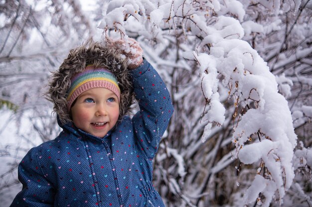 Kleines schönes Mädchen in Winterkleidung, das allein mitten in einem verschneiten Wald steht