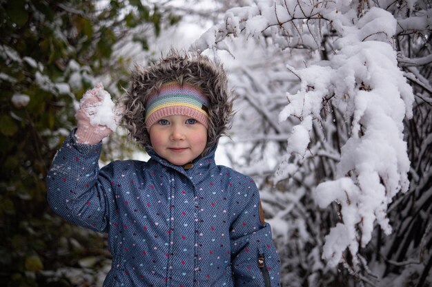 Kleines schönes Mädchen in Winterkleidung, das allein mitten in einem verschneiten Wald steht