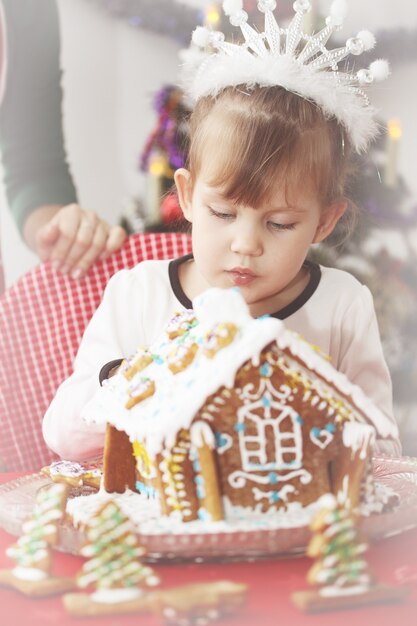 Kleines schönes Mädchen schmückt Lebkuchenhaus zu Weihnachten