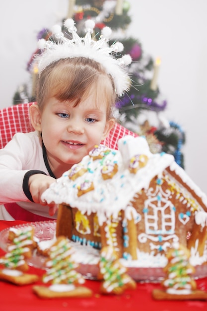 Kleines schönes Mädchen schmückt Zuckerguss-Lebkuchenhaus