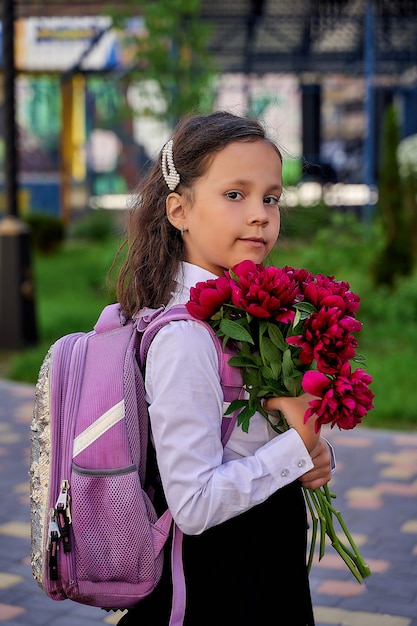 Foto kleines schönes schulmädchen in einem weißen hemd mit blumen.