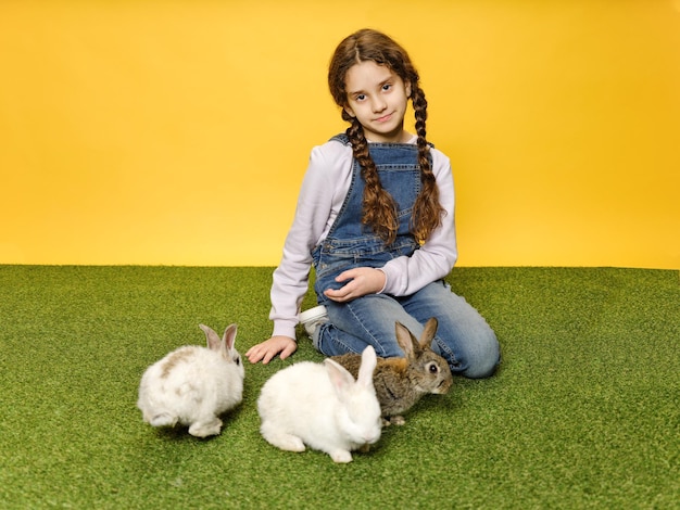 Kleines Schulmädchen legt sich hin und spielt mit den Hasen im gelben Hintergrund des Studios