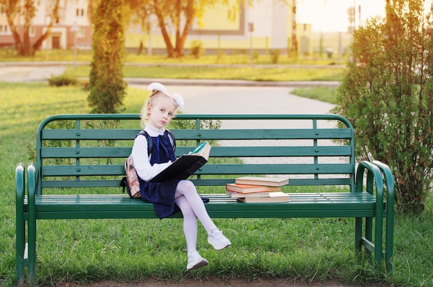 Kleines Schulmädchen mit Büchern, die auf Bank sitzen