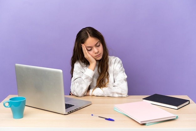 Kleines Studentenmädchen an einem Arbeitsplatz mit einem Laptop auf violettem Hintergrund mit Kopfschmerzen with