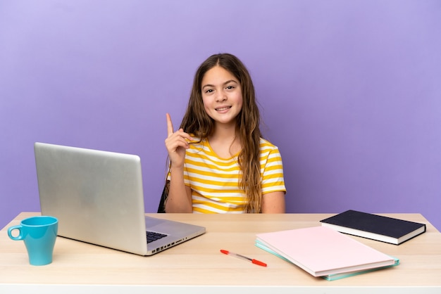 Kleines Studentenmädchen an einem Arbeitsplatz mit einem Laptop, der auf violettem Hintergrund isoliert ist und einen Finger im Zeichen des Besten zeigt und hebt