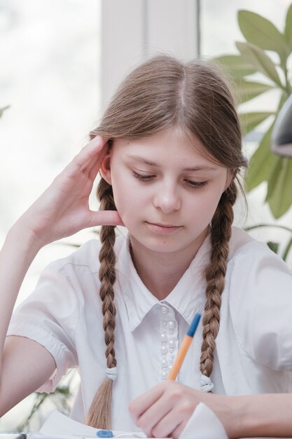 Kleines Studentenmädchen, das in der Schule studiert. Hobby zu Hause. Lächelndes Kindermädchen, das zu Hause malt. Vom Lehrer erzogen werden vs. zu Hause mit den Eltern lernen und lernen. Junges Mädchen, das Hausaufgaben macht.