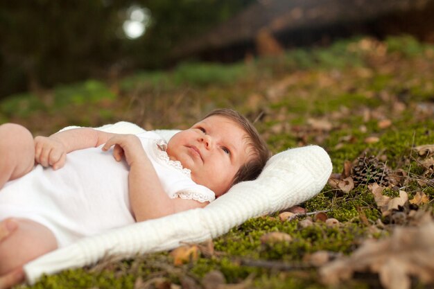 Kleines süßes Baby in weißer Kleidung, das auf der weißen Decke auf dem Gras liegt