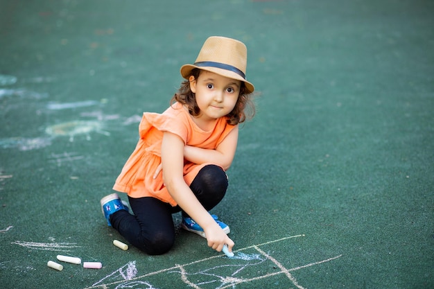 Kleines süßes glückliches Mädchen malt eine Kreide auf Asphalt auf dem Boden auf dem Spielplatz Kreative Sommeraktivität für Kinder
