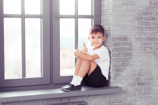 Kleines süßes Kindermädchen in weißer Tanzform, das am Fenster im modernen Tanzstudio sitzt