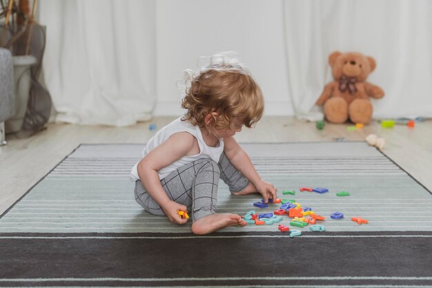 Kleines süßes Kleinkind, das mit Spielzeugbuchstaben spielt, die auf dem Boden sitzen