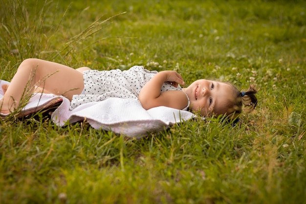 Kleines süßes Mädchen 1-3 in einem leichten Kleid liegt im Sommer auf einem Plaid in einem Feld von Roggenährchen