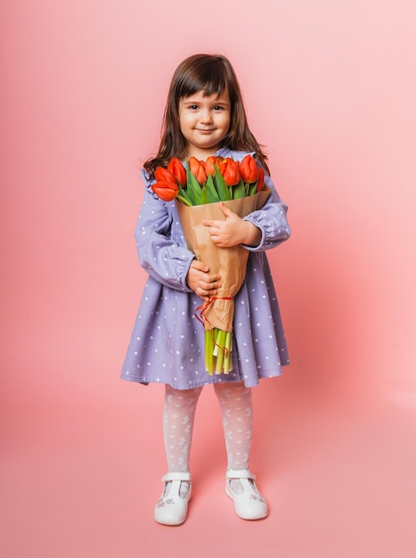 Kleines süßes Mädchen, das einen Strauß Tulpen in handwerklicher Verpackung auf rosa Hintergrund hält Glücklicher Frauentag Platz für Text