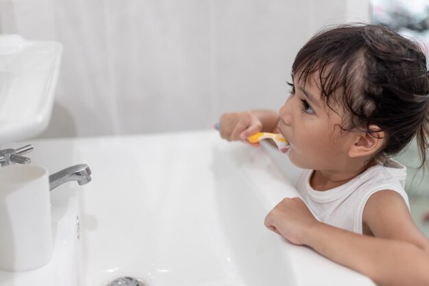 Kleines süßes Mädchen, das ihre Zähne mit einer Zahnbürste im Badezimmer putzt