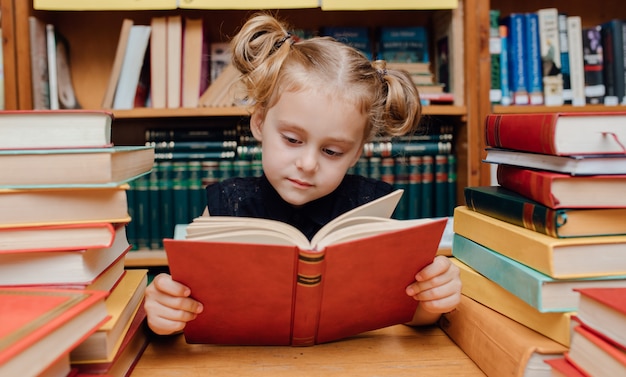 Kleines süßes Mädchen, das in der Bibliothek liest