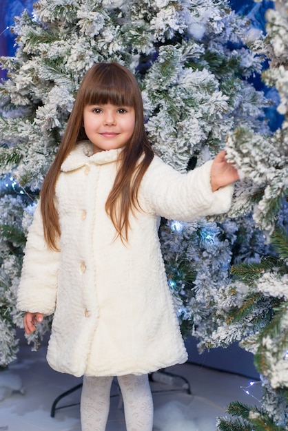 kleines süßes Mädchen, das nahe Tannenbaum aufwirft